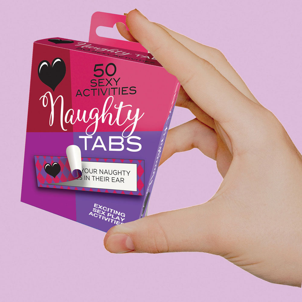 A hand presents a Naughty Tabs - Sexy Suggestions - Set of 50 box, promising thrilling sexual activities. The pink and purple heart-adorned packaging hints with a card labeled IN THEIR EAR, framed by a light purple backdrop for seductive allure.