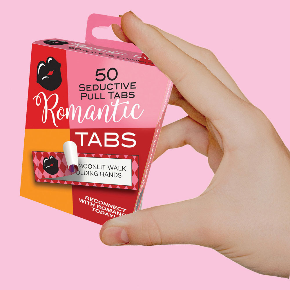 A hand holds a box of Romantic Tabs - Romantic Suggestions - Set of 50, featuring hearts in pink and red. One tab suggests a Moonlit Walk Holding Hands. The tagline encourages rekindling romance with playful activities today for unforgettable moments.