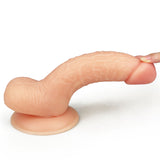 A hand touches the tip of The Ultra Soft Dude - Flesh 17.8 cm (7) Dong, a realistic, ultra-soft dildo made from flesh-toned silicone. Its textured details and curved shape are showcased against a white background, with its wide, round base ensuring stability as its slightly stretched.