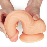 Someone is holding The Ultra Soft Dude - Flesh 20.3 cm (8) Dong, a skin-toned silicone dildo with a flexible, textured surface, curved cylindrical shape, and wide suction cup base for adult use, set against a plain white background.