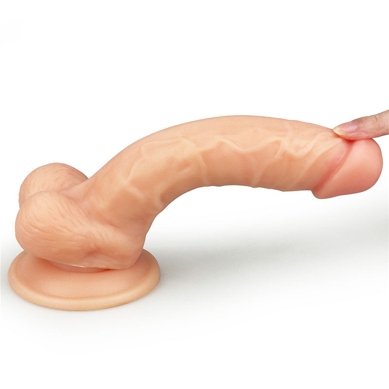 A persons fingers hold the tip of The Ultra Soft Dude - Flesh 20.3 cm (8) Dong, a realistic silicone dildo with a veined texture. It has a flared suction cup base, bends slightly, and sits securely on a surface.