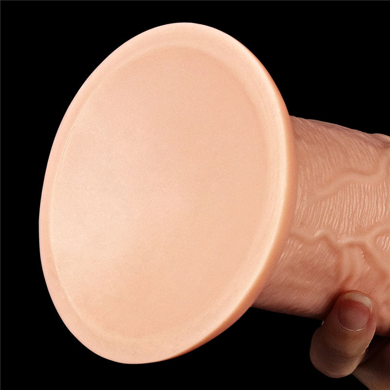 Close-up of a person holding the King Size 11 Realistic Dildo - Flesh 28 cm Dong with a round suction cup base against a black background. The base is smooth, while the textured cylindrical body features lifelike ridges and veins for added realism.