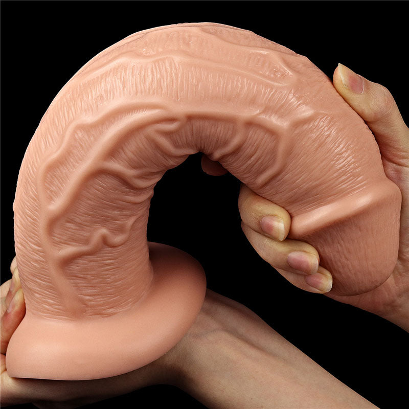 A hand holds the King Size 11 Realistic Dildo - Flesh 28 cm Dong, featuring a textured tentacle-like design with intricate vein details. Its flexible with a bent-forward shape and a suction cup base, set against a solid black background.