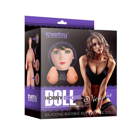 The image shows the packaging for the Victoria Horny Boobie Doll - Inflatable Love Doll by Lovetoy. The box features images of the doll and a model in black lingerie, emphasizing its realistic silicone breasts with text promoting the affordable love doll.