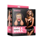 The Victoria Horny Boobie Doll - Inflatable Love Doll by Lovetoy comes in packaging featuring lifelike images of the doll, showcasing its realistic silicone breasts and open mouth. The boxs black and pink branding highlights its authenticity with descriptive text.