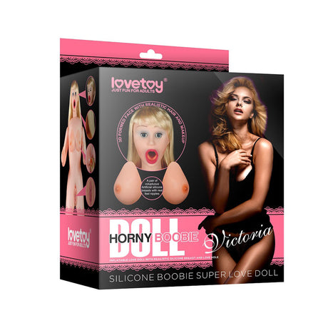 The Victoria Horny Boobie Doll - Inflatable Love Doll by Lovetoy comes in packaging featuring lifelike images of the doll, showcasing its realistic silicone breasts and open mouth. The boxs black and pink branding highlights its authenticity with descriptive text.