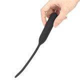 A hand holds the Ultimate Silicone Vibrating Urethral Dilator, designed in black silicone with an elongated, narrow, and flexible shape tapering from a thicker handle to a thinner end, perfect for deep penetration in therapeutic contexts. The background is plain white.