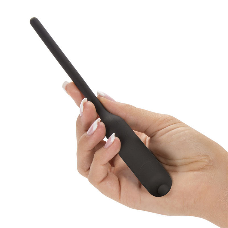 A hand with French tip nails holds the Ultimate Silicone Vibrating Urethral Dilator - Black Vibrating Urethral Sound, featuring a slim design and rounded base. The plain white background emphasizes the devices purpose for deep penetration.