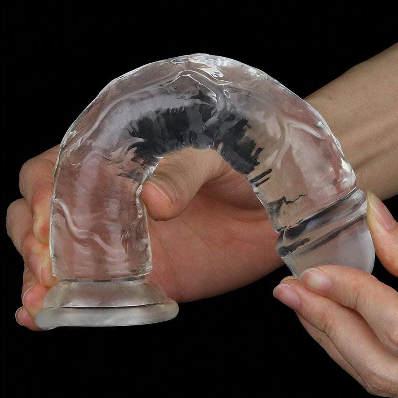 Two hands hold a skin-safe, transparent Flawless Clear Dildo 7 from the LOVETOY Shameless Clear Series, featuring a textured rubber-like surface. This cylindrical dong bends into an arch against a black background, highlighting its flexibility and innovative design.