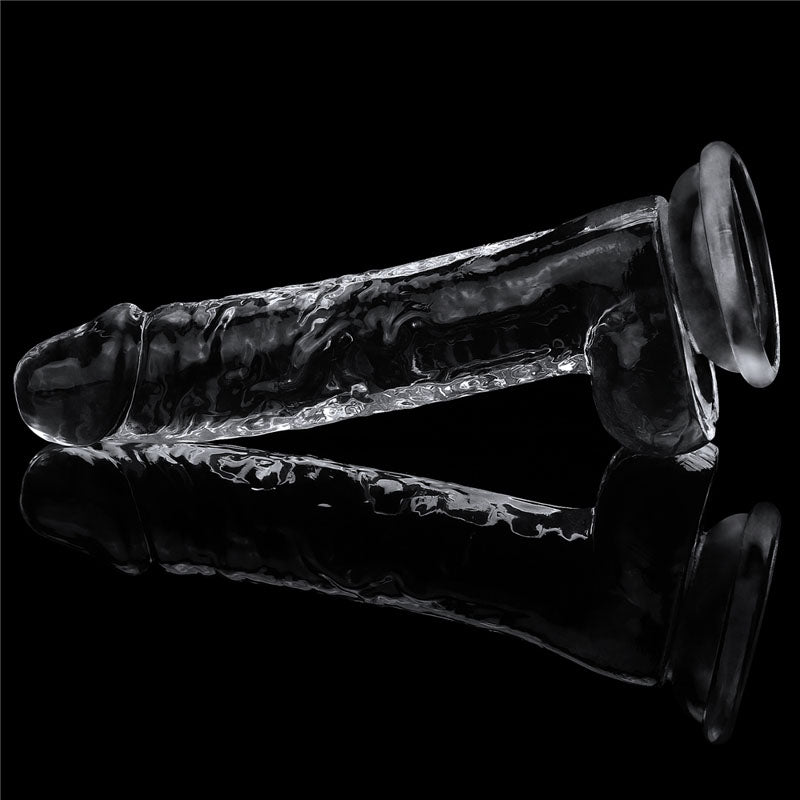 The Flawless Clear Dildo 7.5, part of the LOVETOY shameless clear series, is a skin-safe transparent 19 cm dong with a phallic shape. It rests horizontally against a black background, featuring a smooth texture, slight curve, and suction cup base for stability, with reflections enhancing its intricate details.