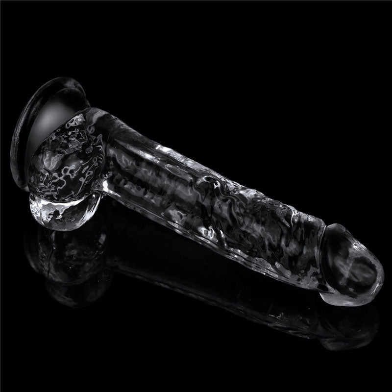 The Flawless Clear Dildo 7.5 from the LOVETOY Shameless Clear Series rests elegantly on a reflective black surface, featuring swirling marbled patterns and a flared base for stability. This artistic, skin-safe transparent toy is visually striking and phallic in shape.