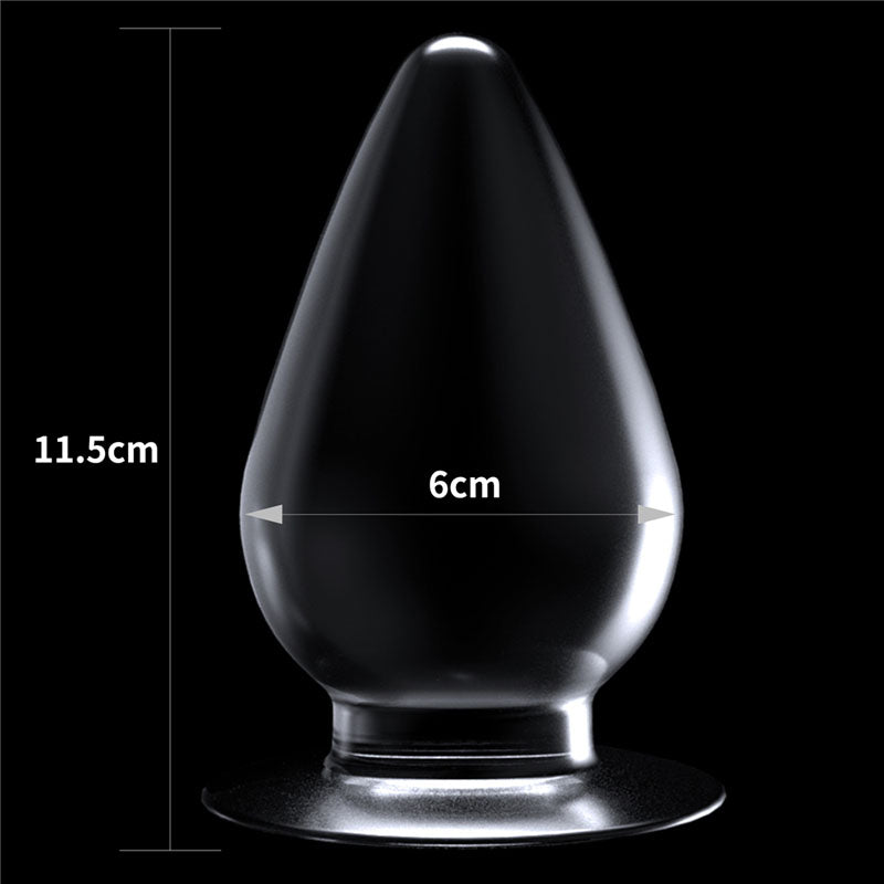 The Flawless Clear Anal Plug, shaped like a transparent teardrop with a flat circular base, measures 11.5 cm tall and 6 cm wide at its widest point. It is set against a black backdrop with dimensions marked on the image.