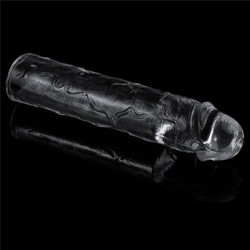 The Flawless Clear Penis Sleeve 2 is a clear TPE cylindrical sculpture with intricate surface textures. Lying horizontally on a reflective black surface, it showcases an authentically realistic appearance and smooth finish.