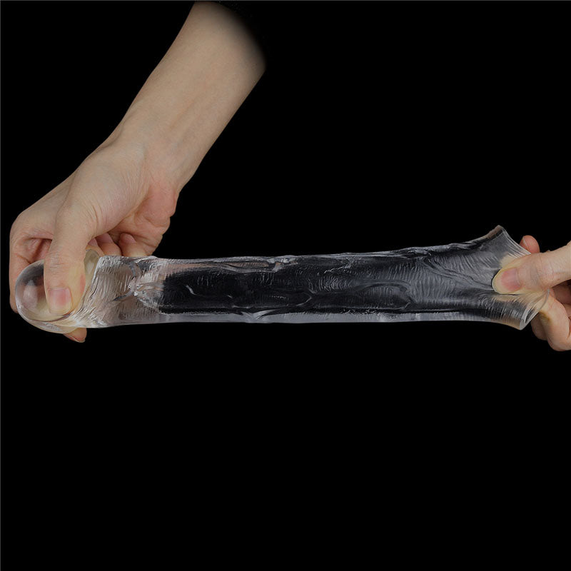 Two hands stretch the Flawless Clear Penis Sleeve 2, a translucent, cylindrical TPR object, against a dark backdrop, showcasing its flexible nature as light reflects off its shiny surface.