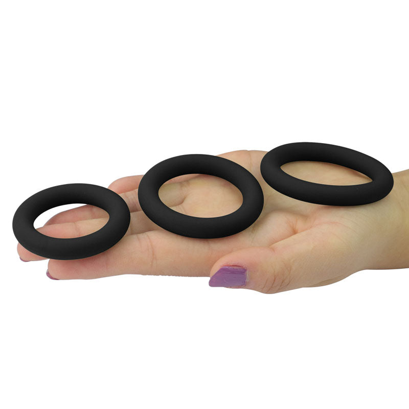 A hand with painted nails holds the Power Plus Soft Silicone Snug Ring set, featuring three black cock rings of different sizes. Positioned side by side against a plain white background, their minimalist design enhances stronger erection and delays ejaculation.