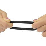 Hands with purple nail polish stretch a black, oval-shaped resistance band horizontally, resembling the flexibility of the Power Plus Soft Silicone Snug Ring. The plain white background highlights the focus on the hands and the resistance band.