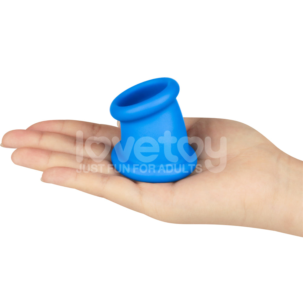 A hand holds a small silicone toy, featuring a cylindrical design with a wide opening. The brand name lovetoy and slogan just fun for adults overlay the image. The Pinnacle Pro Tapered Squeeze - Blue Ball Stretcher is your discreet companion against a plain white background.