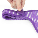 A hand holds a corner of the Ingen Easy Strap-On Harness, a purple fabric with white dots. Its plush texture and thick edges offer comfort. The adjustable velcro ensures a snug fit against the plain white background.