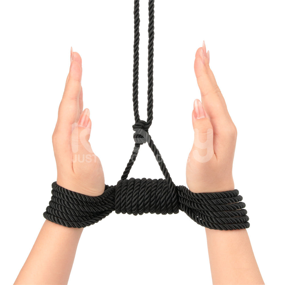 Two hands are tied with Rebellion Reign Silky Bondage Rope in black, palms facing inward. The fingers are extended with neat nails. Premium polyester loops above the wrists extend upward. The white background contrasts starkly with the black ropes ebony hue.