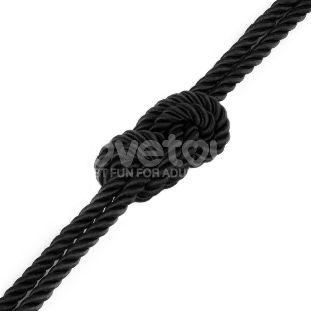 A Rebellion Reign Silky Bondage Rope - Black lies intricately knotted against a plain white background. This premium black bondage rope, tightly coiled, highlights the texture and detail of its twisted polyester fibers in a 10-meter length.