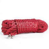 A neatly coiled Rebellion Reign Silky Bondage Rope in vibrant red lies on a white surface. Crafted from premium polyester, the rope features a thick, twisted texture with metallic silver caps on both ends, and its glossy sheen highlights its tightly wound structure. .