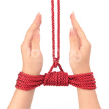 Two hands with long nails are tied together using the Rebellion Reign Silky Bondage Rope, crafted from premium polyester. The red rope extends upward out of frame, intricately knotted with palms facing each other against a plain white background.