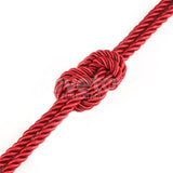 A red Rebellion Reign Silky Bondage Rope, made of premium polyester strands, is tied into a symmetrical knot on a white background. The knot is centered in the image, with the 10-meter rope extending out of the frame on both sides.