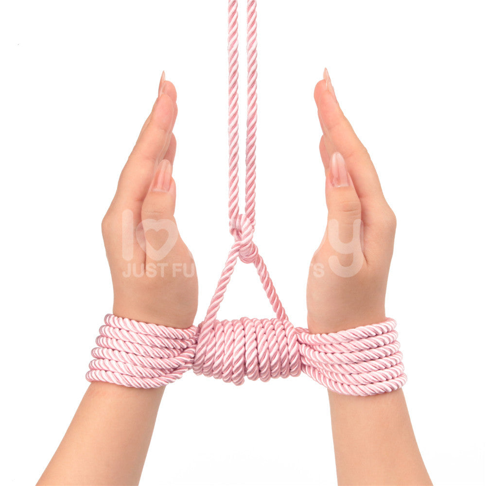 Two hands are bound together using the Rebellion Reign Silky Bondage Rope in pink, tied securely around the wrists. The ropes silky finish suggests suspension, set against a plain white background emphasizing the hands and intricate bondage design.