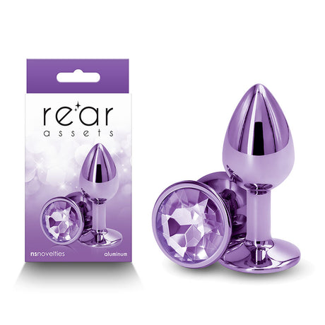 The image shows the Rear Assets Small Butt Plug in purple aluminum with a round gem base, next to its packaging. This stylish and body-safe anal toy features an enchanting design, highlighted by its jewel-like detail.