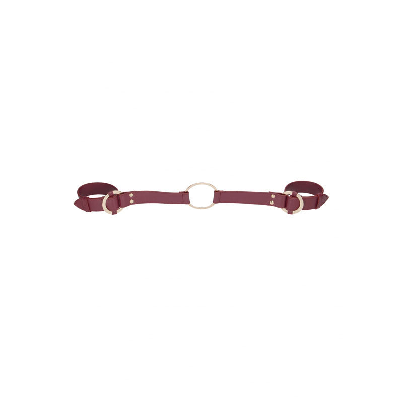 The OUCH! Halo - Handcuff With Connector in burgundy features two side buckle straps and a central gold metal ring, showcasing a minimalist design. The metallic accents add allure, making it perfect for enhancing any BDSM kit against a plain white background.