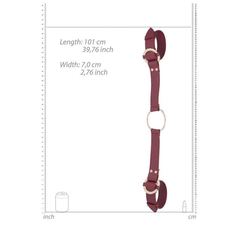 The OUCH! Halo - Handcuff With Connector in burgundy features a maroon leather strap with metal loops, an adjustable buckle, and a central ring. It measures 101 cm (39.76 inches) in length and 7 cm (2.76 inches) in width, shown alongside a scale bar with a soda can and bullet for size reference.