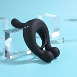 The Playboy Pleasure TRIPLE PLAY, a black USB rechargeable cock ring with a wireless remote, is crafted from body-safe silicone. It features round ends, charging port, and indicator lights, set against a light blue background with transparent geometric acrylic blocks for a modern vibe.