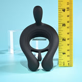 The Playboy Pleasure TRIPLE PLAY, a black silicone toy with an O-shaped structure and small protrusion, features vibrating motors. Positioned upright beside a yellow ruler showing its 5-inch height, it stands against a soft blue backdrop with a clear acrylic block.