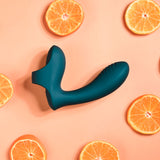 The Playboy Pleasure WRAPPED AROUND YOUR FINGER - Green USB Rechargeable Finger Stimulator, featuring a bulbous end and ribbed surface for multi play and G-Spot or P-Spot stimulation, is centered on a peach background with evenly spaced orange slices, creating a balanced and modern visual.