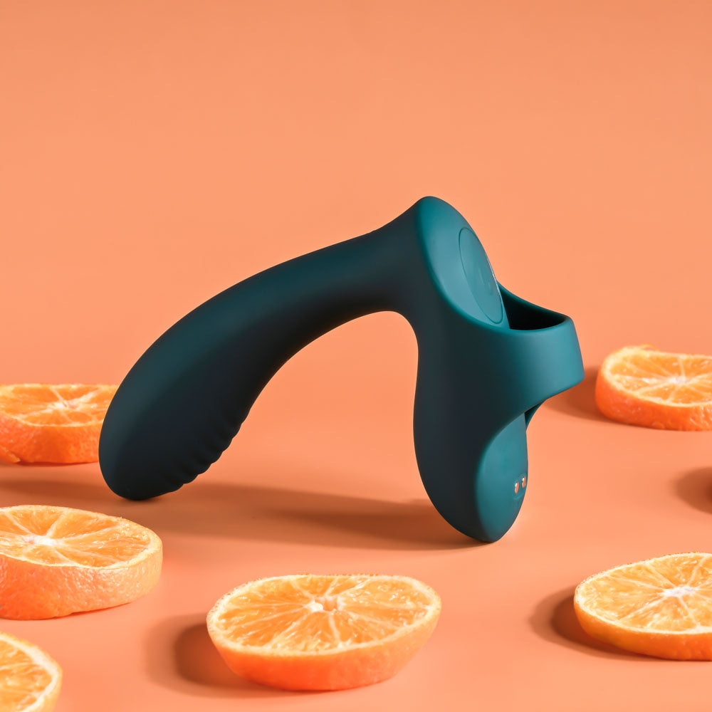 A green Playboy Pleasure finger stimulator with a sleek, ergonomic design stands upright on an orange surface. Surrounded by halved oranges, it exudes vibrancy and freshness against the matching backdrop, reminiscent of a multi-play gadget.