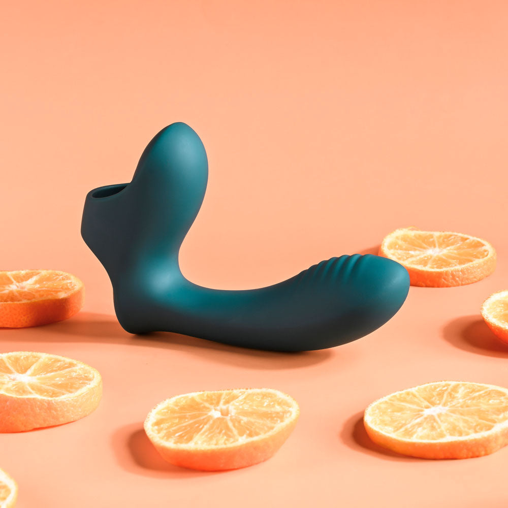 A green Playboy Pleasure WRAPPED AROUND YOUR FINGER USB Rechargeable Finger Stimulator with a textured tip is centered on a peach background. Orange slices encircle it, creating vibrant contrast and highlighting its sleek design and matte finish.