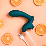 The Playboy Pleasure WRAPPED AROUND YOUR FINGER, a dark teal USB rechargeable finger stimulator for versatile G-Spot and P-Spot use, is artistically surrounded by half-sliced oranges against a light peach background.