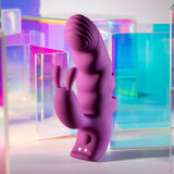 The Playboy Pleasure LEND A HAND, a purple USB rechargeable finger vibrator, features dual motors for G-Spot exploration and a bunny-shaped clitoral stimulator. Its ergonomic shape and body-safe silicone finish are highlighted against colorful translucent geometric shapes in pink, blue, and purple hues.