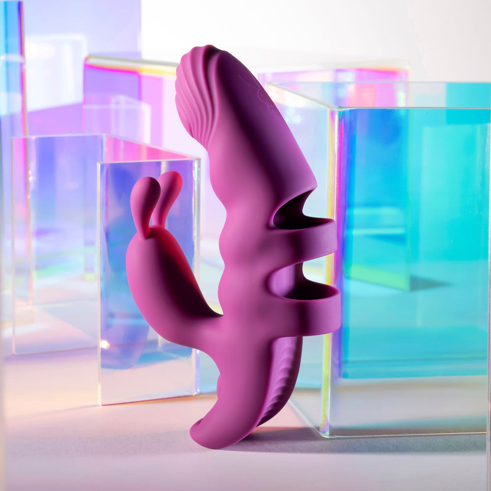 The Playboy Pleasure LEND A HAND - Purple USB Rechargeable Finger Vibrator, crafted from body-safe silicone with dual motors and unique dual arms for G-spot exploration, stands upright amidst colorful, translucent geometric shapes in blues, purples, and greens for a modern aesthetic.