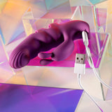 The Playboy Pleasure LEND A HAND - Purple USB Rechargeable Finger Vibrator, made of body-safe silicone with a textured shaft, is placed on a holographic surface with a looped USB charging cable. Geometric acrylic shapes and pastel rainbow reflections form the vibrant background.