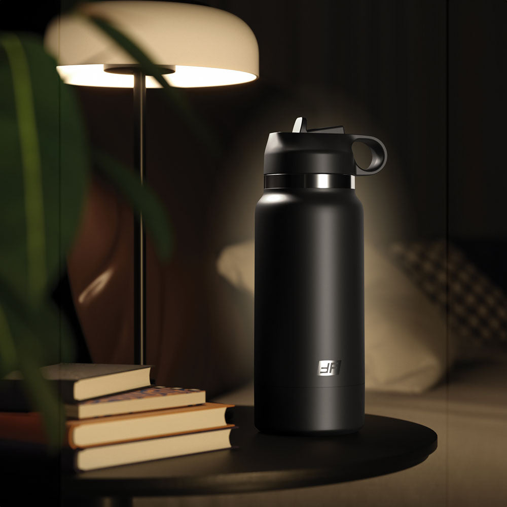 The PDX Plus Fap Flask - Thrill Seeker sits on a round, dark table, surrounded by books with a modern lamp casting a cozy glow. In the background, a plush pillow and sofa corner complete the inviting scene.