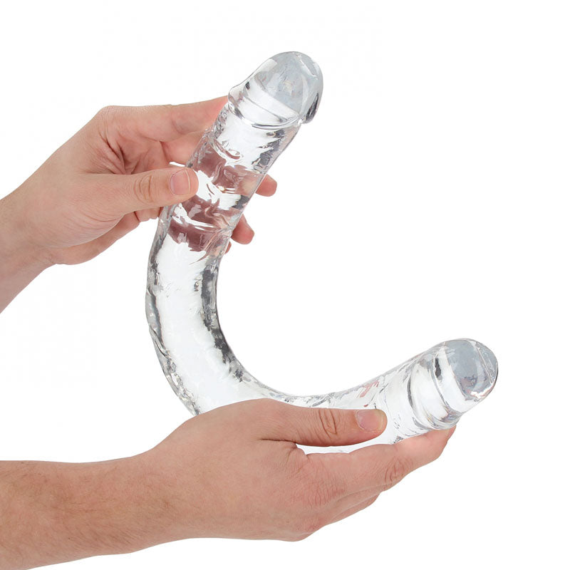 Two hands hold the REALROCK 45 cm Double Dong, a transparent, double-ended glass object with textured sides and rounded tips. Designed for finger-like precision, it is slightly curved to showcase its body-safe flexibility and innovative design.