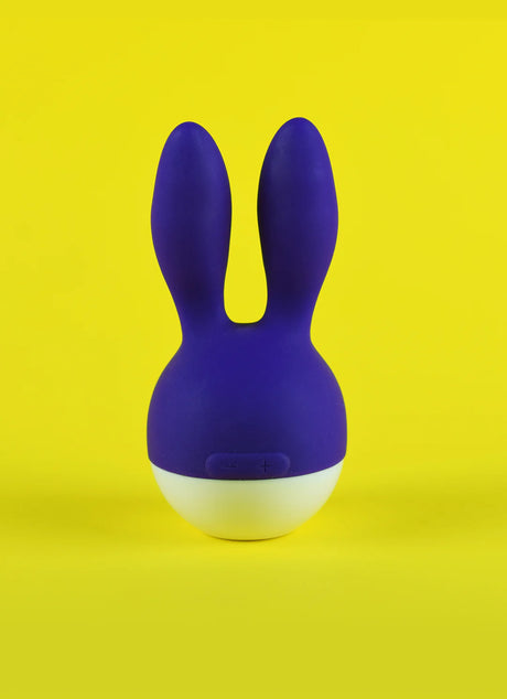 A purple, rabbit-shaped item with two upright ears and a white base is centered against a bright yellow background. The design is simple and modern, resembling a toy or decorative object.