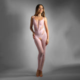 Wearing the SHEER FANTASY DREAM COME TRUE in baby pink, a person with long hair poses confidently against a gray background. This form-fitting, sleeveless bodysuit features fishnet detailing and cut-outs, elegantly paired with high-heeled sandals. One hand rests on their hip while the other hangs relaxed.