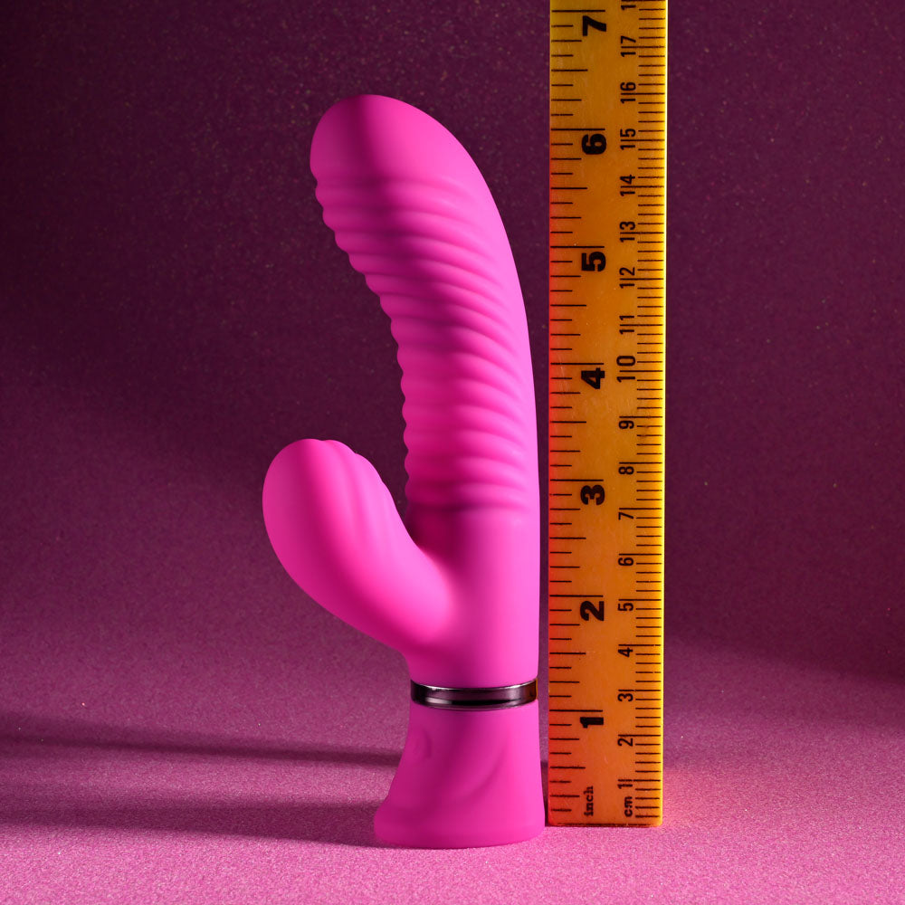 The Selopa NEXT WAVE - Pink 16.4 cm USB Rechargeable Dual Vibrator has powerful motors, a ribbed texture, and rabbit ear extensions, all showcased against a glittery pink background with silver ring details near the base. A yellow tape measures its height at approximately 6 inches.