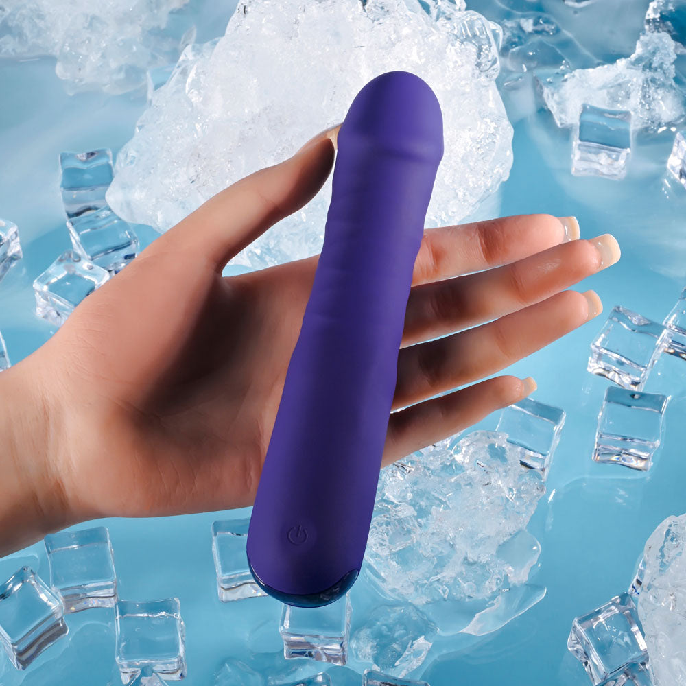 A hand holds the Selopa AMBITION, a purple 17 cm USB rechargeable thrusting vibrator with a visible power button at the base. The background features ice cubes scattered on a blue surface, suggesting coolness and refreshment.