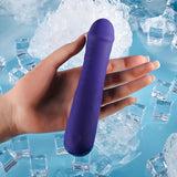 A hand holds the Selopa AMBITION, a purple 17 cm USB rechargeable thrusting vibrator with a visible power button at the base. The background features ice cubes scattered on a blue surface, suggesting coolness and refreshment.