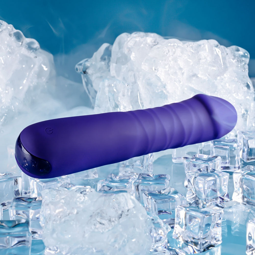 The Selopa AMBITION, a 17 cm USB rechargeable thrusting vibrator in purple with a smooth, slightly rippled surface, lies amidst scattered clear ice cubes. Made from phthalate-free silicone with a power symbol, its sleek design contrasts refreshingly against the blue background.