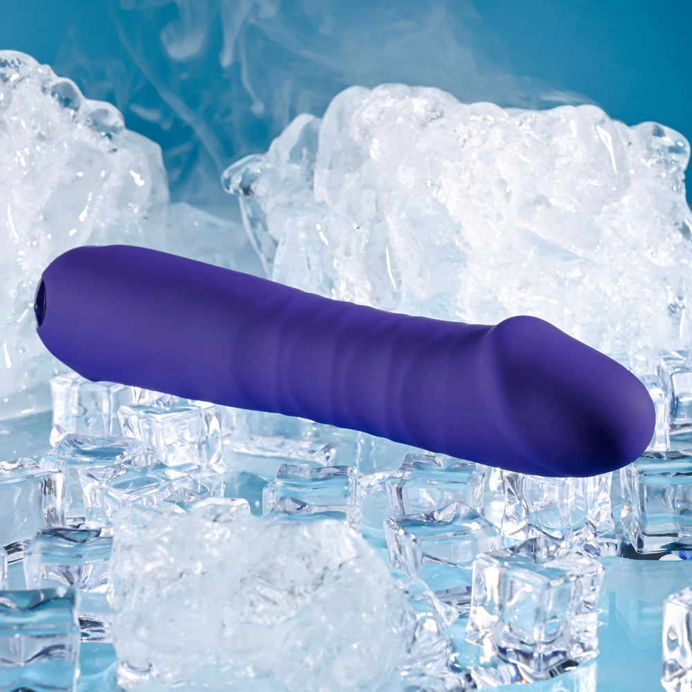 The Selopa AMBITION - Purple 17 cm USB Rechargeable Thrusting Vibrator rests on a reflective surface, surrounded by ice cubes against a blue backdrop, accentuating the contrast between the massagers warm hue and the cool environment.