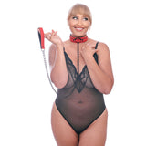 A woman in a sheer black lace bodysuit wears the Sex & Mischief Amor Collar and Leash - Red Restraint, made of vegan leather. Her blonde hair is in a ponytail as she smiles holding the chain handle, against a white background, evoking intoxicating sensations.